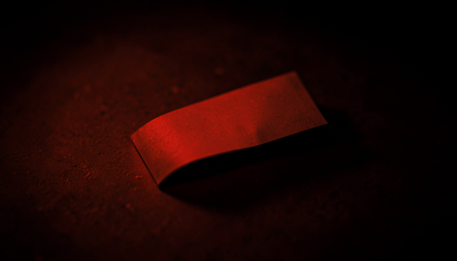 Atmospheric orange-tinted photograph of a single folded paper slip on a warm dark surface, soft shadow and dim ambient light